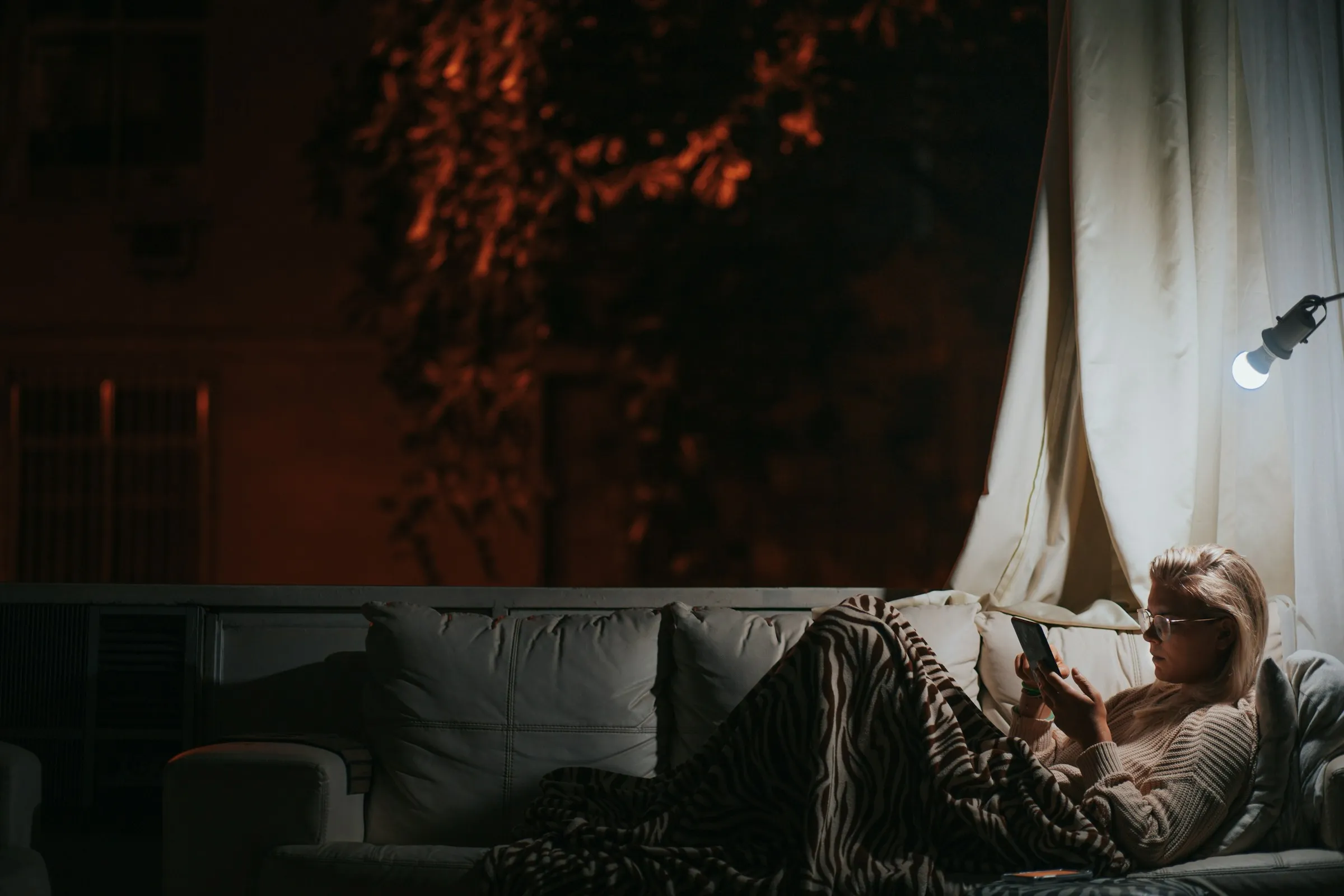 A woman relaxing on a sofa in the evening, reading on her phone